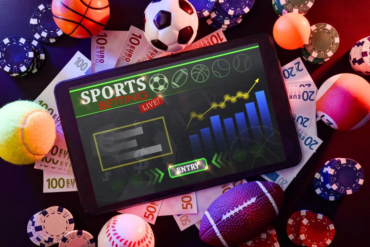 iPad mit geöffneter Website für ausländische Wettanbieter liegt auf einem Haufen aus Geldscheinen neben verschiedenen Spielbällen