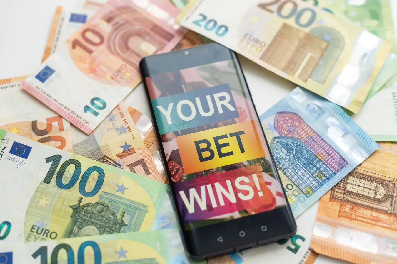 Smartphone auf einer Menge an Euro-Scheinen als Symbol für Sportwetten Bonus