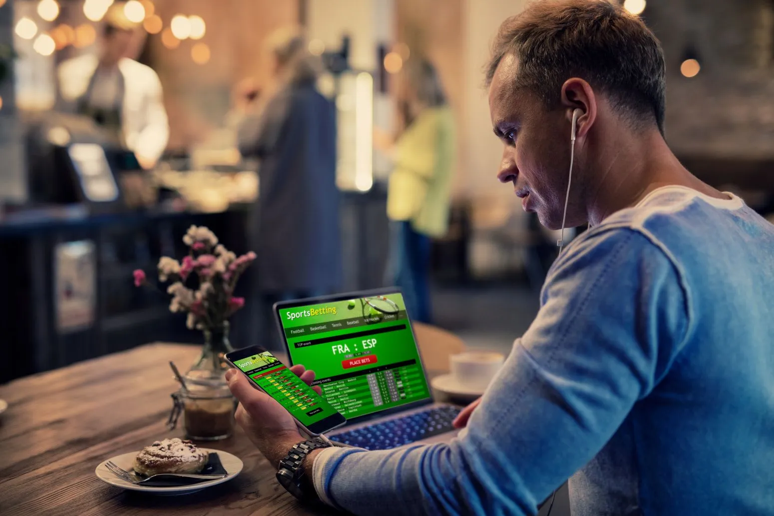 Mann spielt auf mehreren Endgeräten Sportwetten